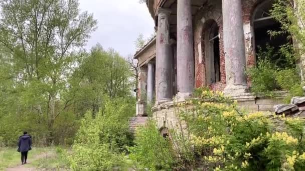 Ein Mann geht langsam neben einem alten, vergessenen Anwesen — Stockvideo