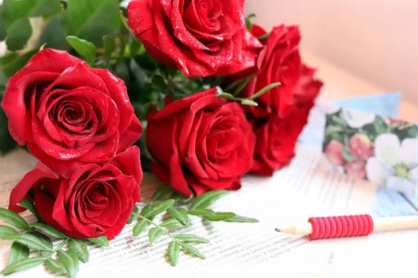 엽서와 연필 뒤에 붉은 장미 꽃다발이 놓여 있는 모습 — 스톡 사진