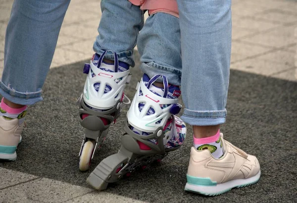 mom in light jeans and sneakers teaches daughter in jeans and roller skates to roller skate feet in shoes