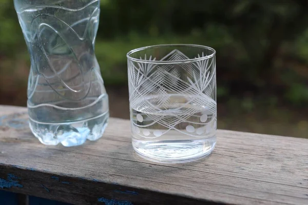 在绿油油模糊的背景下 用玻璃杯盛于木制表面的塑料瓶水 — 图库照片