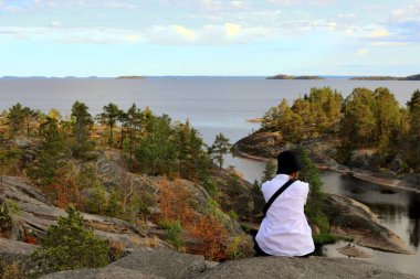 girl tourist in a white shirt and black panama sits admiring the views of the skerries, the rocky islands of Lake Ladoga on a summer day