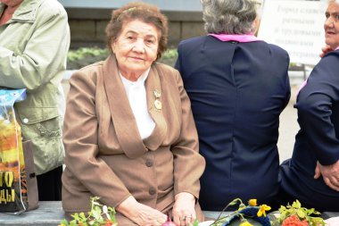 diğer yaşlı kadınlar arka plan üzerinde bir bankta oturmuş bir madalya ile kahverengi elbiseli yaşlı bir kadın