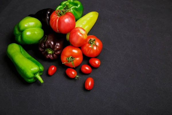 Multicolored farm vegetables on a black background, space for text