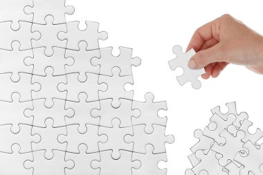 Beyaz arka planda izole edilmiş yığınlardan seçilen beyaz yapboz parçalarını birleştirmeye çalışan insan eli. Çözüm stratejisi imajı bulmaya çalışırken veya yapboz yaparken. yeniden inşa, yeniden inşa