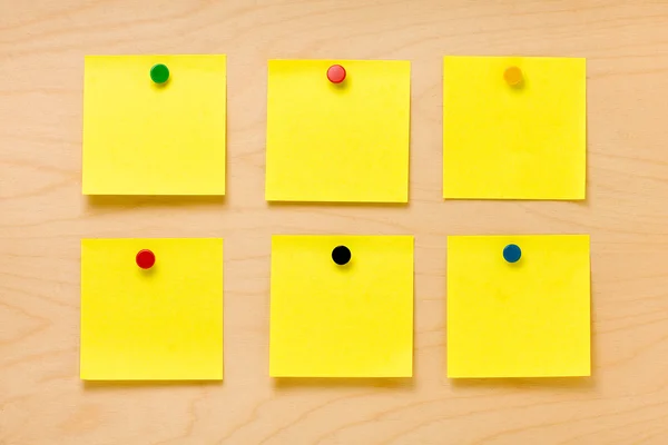 Notas postit en blanco amarillas cuadradas bien ordenadas colocadas por alfileres de colores en un tablero de madera — Foto de Stock