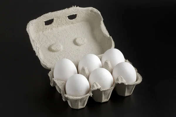 Seis huevos blancos enteros en un contenedor de dibujos animados abierto sobre fondo negro —  Fotos de Stock