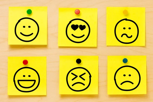 Ruční kresba emotikony na šesti žluté postit poznámky přiložené barevné kolíky na dřevěném prkénku — Stock fotografie