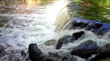 Suyun güzel hareketi, sıçrama, köpük. Yeşil bitkilerin ve gökyüzünün yansıması.