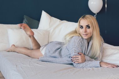 Güzel ve genç kadın yatakta gri süveterli