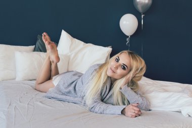 Güzel ve genç kadın yatakta gri süveterli