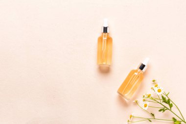 Cam esans şişeleri ya da papatya çiçekli serum. Pembe arka planda nemlendirici yüz kremi ve papatya.