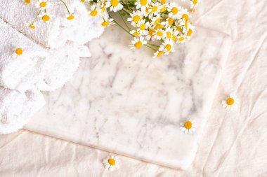 Kozmetik ürünleri reklamı için podyum. Havlular ve mermer tahtada papatya çiçekleri. Yüz kremi ve papatya çayı.
