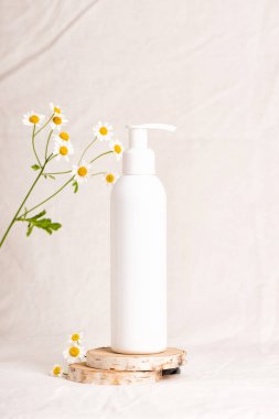 Plastik losyon ya da sabun şişesini fotokopi alanı olan tahta dilimlere pompala. Nemlendirici el kremi ve papatya çiçeği. Güzellik kozmetik ürünlerinin maketi. Bej kumaş arkaplanı