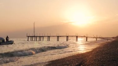Deniz dalgaları, kumsal ve altın gün batımında iskele. Türkiye 'de yaz tatili
