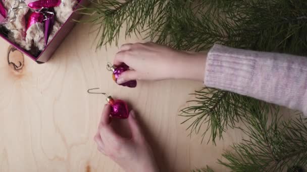 女性的手拿着一盒老式圣诞树装饰品和松树枝条 放在轻型木制背景上 — 图库视频影像
