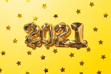 2021 altın balon, tebrik şapkası ve sarı kağıtta altın yıldız konfetisi. Noel ya da yeni yıl festivali konsepti. Üst görünüm ve düz uzanma.