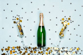 Láhev šampaňského a flétny s černými a zlatými hvězdami a kruhové konfety na modrém pozadí. Vánoce, Nový rok nebo narozeniny nebo svatební slavnostní koncept. Horní pohled a byt ležel.