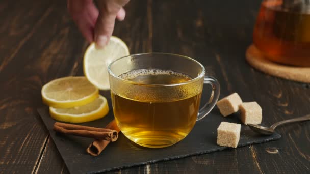 Glass cup of hot ginger tea with lemon on dark wooden table. — Stock Video