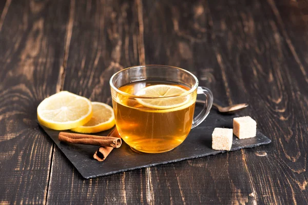 Glass cup of hot ginger tea with lemon on dark wooden table. — Stock Photo, Image