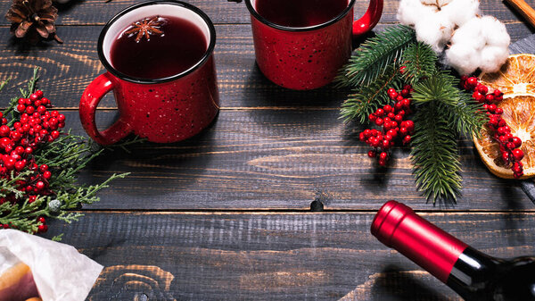 Bottle, mugs and ingridients for mulled wine on wooden dark table