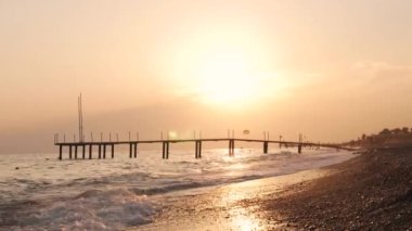 Deniz dalgaları, kumsal ve iskele altın gün batımında.