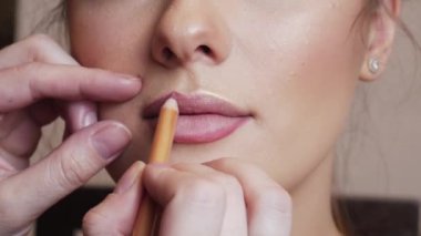 Makyöz kadın dudağına pembe kalem sürüyor.