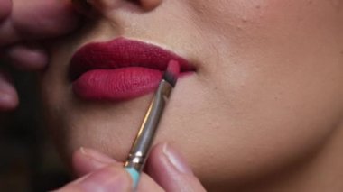 Makyöz kadın dudağına kırmızı ruj sürüyor.