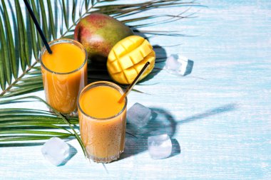 Bir bardak taze mango suyu kokteyli ve palmiye dalları.