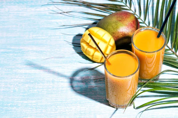 Bir bardak taze mango suyu kokteyli ve palmiye dalları.