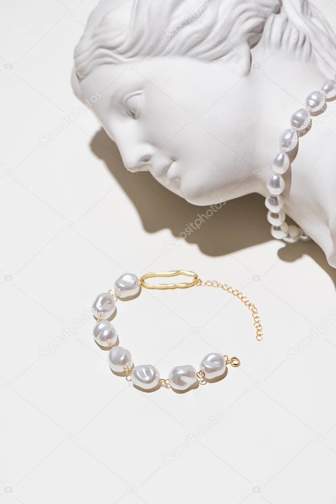 Trendy pearls and gold jewelry on plaster sculpture of woman face