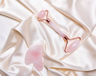 Pembe yeşim yüzlü masaj silindiri ve atlas bej arka planda gua sha.