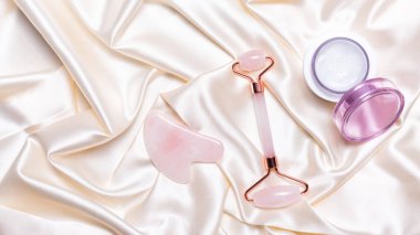 Pembe yeşim yüzlü masaj silindiri ve atlas bej arka planda gua sha.