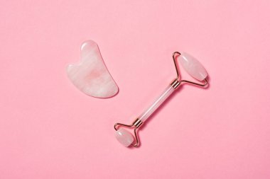 Yeşim yüz masajı silindiri ve pembe arka planda gua sha.