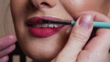 Makyöz kadın dudağına kırmızı ruj sürüyor.