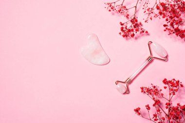 Yeşim yüz masajı silindiri ve pembe arka planda gua sha.