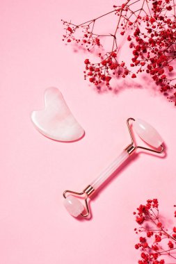 Yeşim yüz masajı silindiri ve pembe arka planda gua sha.