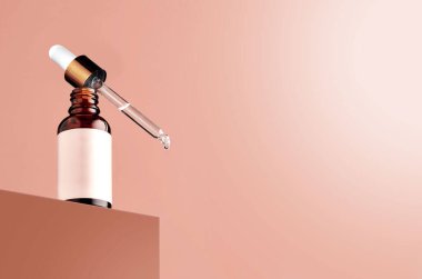 Serum damlacıklı serum şişesi modern, minimal ambalajlı pembe pastel arka planda şişe ve damlatıcıyla çelişiyor. Bir damla sıvı damlatıcının ucunda görünür.