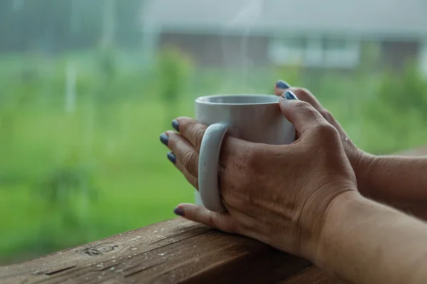 Manos femeninas sosteniendo una taza de café en el día lluvioso — Foto de Stock