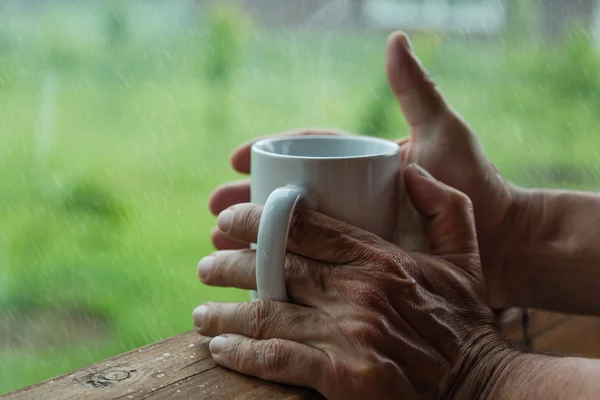Męskie ręce trzymając kubek kawy w deszczowy dzień — Zdjęcie stockowe