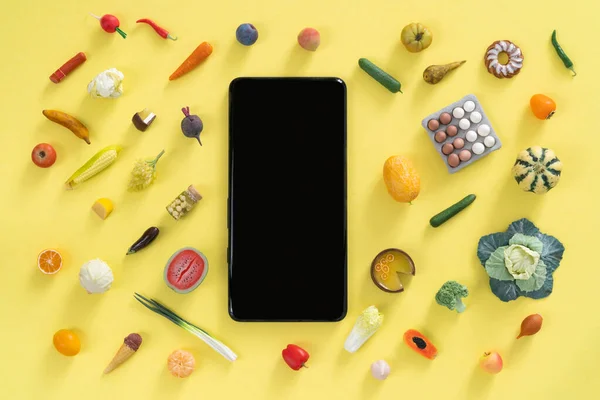 Concepto de compras en línea - diferentes alimentos y teléfono sobre fondo amarillo — Foto de Stock