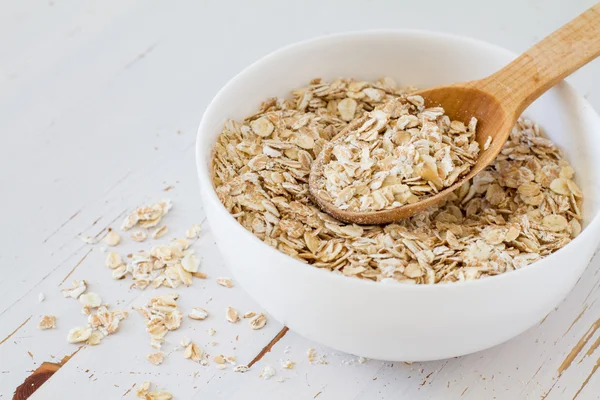 Hafer in weißer Schüssel mit Holzlöffel — Stockfoto