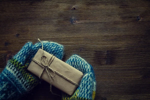 Mano en mitones de punto que sostienen el presente, fondo de madera rústica — Foto de Stock