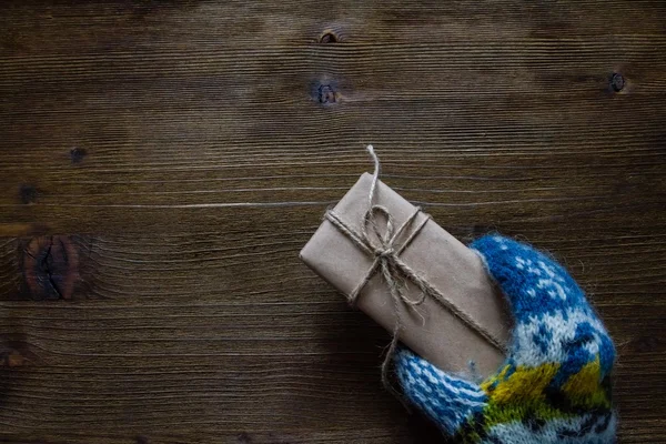 Mano en mitones de punto que sostienen el presente, fondo de madera rústica — Foto de Stock