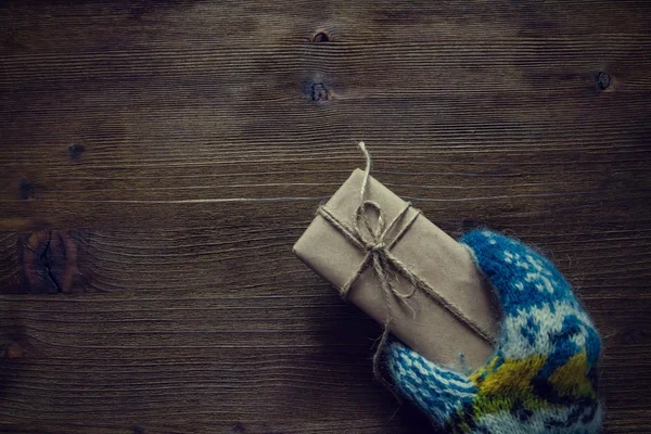 Mano en mitones de punto que sostienen el presente, fondo de madera rústica — Foto de Stock