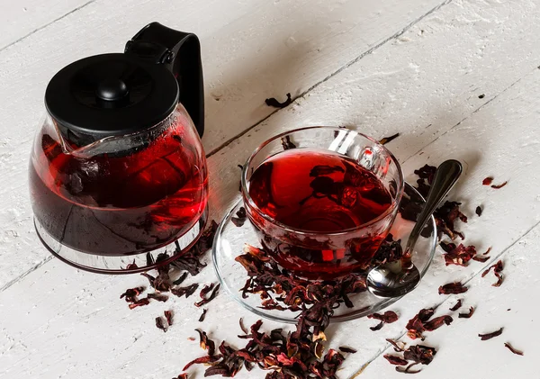 Cup of Karkadeh Red Tea with Dry Flowers and kettle on a wooden