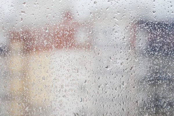 View through a rainy window on a blurred house. Bad rainy autumn weather concept.