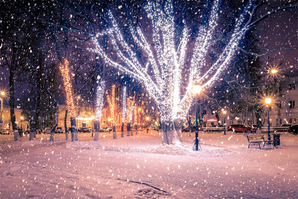 Winter night park with lanterns and Christmas decorations in heavy snowfall.