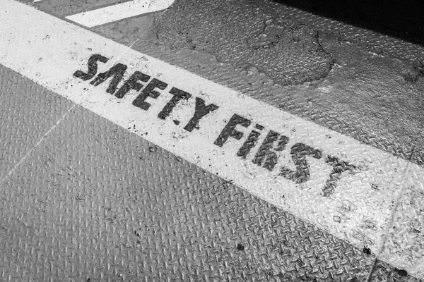 Safety First sign on caution strip,black and white.