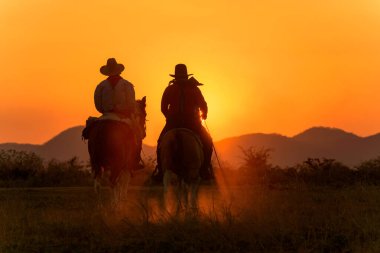 Cowboy riding a horse carrying a gun in sunset with mountain clipart