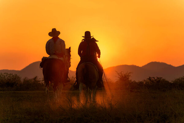 Cowboy riding a horse carrying a gun in sunset with mountain